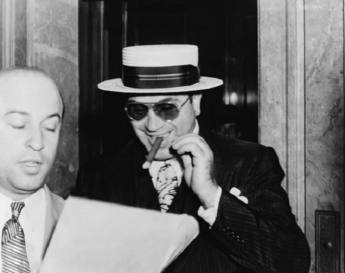 На снимке, сделанном 17 февраля 1931 года в Майами: Аль Капоне с сигарой и широкой улыбкой на лице слушает, как его адвокат Абе Тейтельбаум объясняет, что государство предъявило ему обвинение в уклонение от уплаты налогов