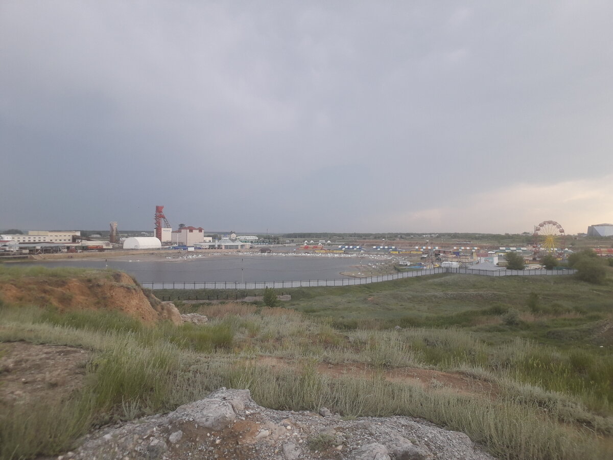 Соль-Илецк показался мне поселком городского типа, частные дома, много где сдают жилье. Все озвучивают цены за место, поэтому за комнату выходит больше🙈. Нашли жилье с красивым видом, на втором этаже, с окна вид на озера, а с лестницы вид на крыши домов.👍 Начало лето выдалось не жарким, на второй день была гроза и дождь лил с вечера и всю ночь. Днем гуляли по окрестностям, рядом продуктовые магазины, готовили сами, у хозяев просторная кухня. Посмотрели на здание тюрьмы Черный дельфин, со стороны.
Удивило, что в начале июня спеет ирга и краснеет вишня. Были на Новом озере, немного покупались, а потом обнаружили надпись, купаться опасно, наверное, из-за подземных шахт. Рядом с озером глыбы соли, немного отбили себе на память.🙃
На третий день пошли на платные озера и там провели весь день, попробовали все по-максимуму, на некоторых запрещено купаться, туда мы не лезли, на больших озерах чего только не плавает - прокладки, бумага, окурки, такое достояние и🙈. На территории бесплатный холодный душ, туда мы не ходили, душ уже приняли в номере. От соли кожу щиплет до боли, лучше смывать. На территории можно купить сувениры и поесть, а также ходят по озеру и предлагают горячую кукурузу и чурчхеллу. До дальних озер, грязевых ходит "тук-тук" и развозит людей. Сама грязь легко намазывается, брать ее надо с дна озера, а смывать ее долго. Соль и грязь.., хорошо, что у нас были с собой бутылки с обычной водой, чтобы помыть руки и лицо, а так рядом с кафе есть краники с водой, где можно умыться, на территории много деревянных будок-туалетов.
За день я сгорела, забыла солнцезащитный крем, в комнате я была похожа на сардельку - красные ноги, плечи, руки, грудь, лицо, кожу не возможно было касаться, пшикала спреем и мазала кремом, ощущение было, что все горит. Остальное время отпуска я уже ходила в кофте и в штанах. Поездка в Соль-Илецк понравилась, ощущение, как будто съездила на юг. За пару дней эффекта от соли я не заметила, обычно сюда приезжают минимум на неделю. Повезло, что народу было еще не так много.😏