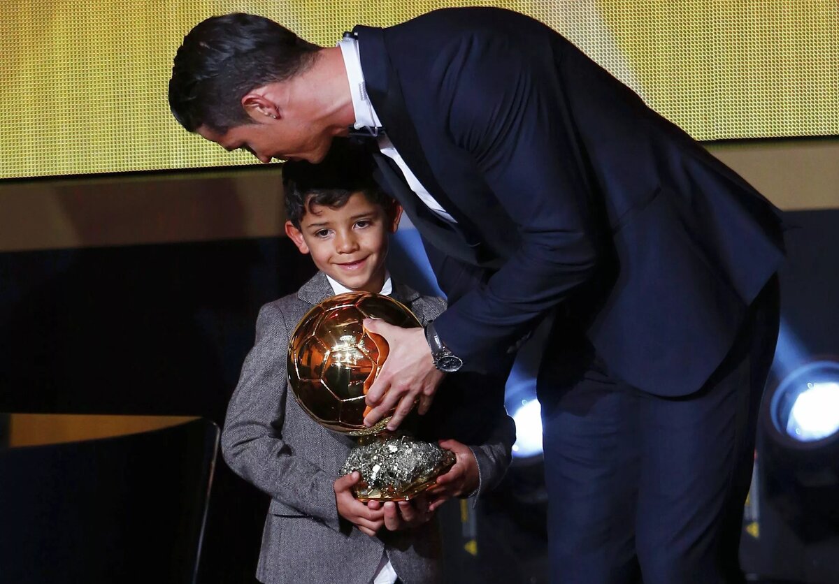 © REUTERS / ARND WIEGMANNПортугальский игрок «Реала» Криштиану Роналду стоит со своим сыном Криштиану Роналду-младшим после того, как выиграл Золотой мяч ФИФА 2014 года во время церемонии награждения футбольных наград в Kongresshaus в Цюрихе 12 января 2015 года.