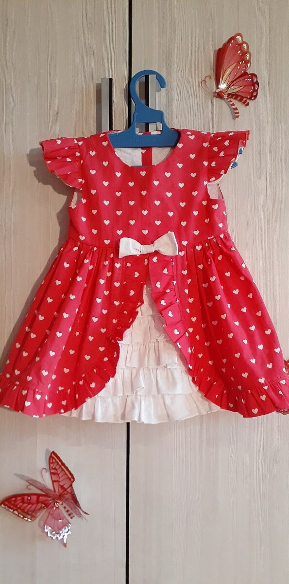Эффектное и при этом несложное платье, которое я сшила для дочки за 1 день. Для пошива на 92 размер потребовался 1 м красного хлопка и 0,5 м белого. Верх платья - это обычная основа, низ - татьянка со сборкой, в центр которой вшита трапеция с оборками. Лиф платья я сделала на подкладке, между основной тканью и подкладкой вшила "крылышки". Застежку выбрала на пуговках, хотя, проще было поставить потайную молнию, но в детских вещах мне больше нравятся именно пуговки, они смотрятся легче и по-детски наивно. Оборки я обрабатывала на оверлоке ролевым швом, если нет оверлока, то на помощь придет тоненький подрубочный шов. Будет еще эффектней, если чередовать оборочки из ткани с кружевом. Нужного метража кружева у меня не нашлось, магазины на тот  момент были закрыты из-за карантинных мер, поэтому обходилась тем, что было дома. А дома была только ткань и пуговки, которые когда-то купила на сдачу. В итоге, платье обошлось мне в 170₽. (1,5м×110₽). 