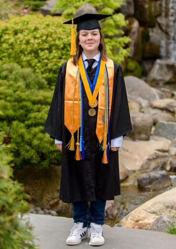 Квадратная академическая шапочка, свисающий с неё шнур с кисточкой, мантия, медальоны на лентах, шнур чести и палантин на плечах Эллиота - это торжественный костюм для выпускной церемонии в США. Цвета шнуров чести обозначают науки, например, золотая кисточка - это общественные и естественные науки.