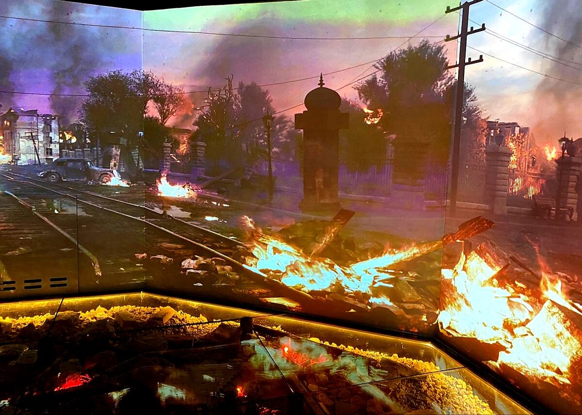 По потолку летят самолёты, в проекции на стенах вокруг вас всё горит и взрывается, воет сирена. И даже под стеклянным полом взрытая земля и обломки кирпичей. 