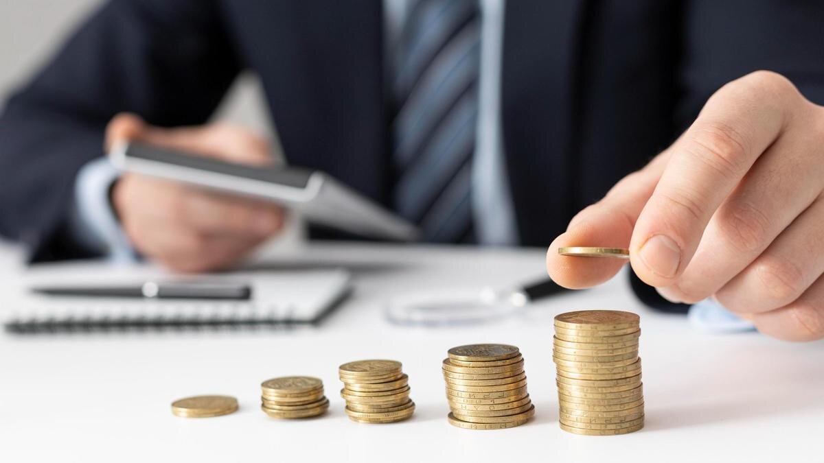    Мужчина в костюме кладет монетку на стопку монет:Freepik