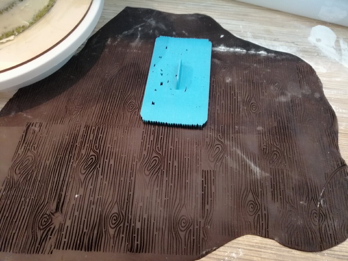 Я присыпала стол сахарной пудрой и раскатала тонко мастику тёмно- коричневого цвета, затем специальной формой придала мастике имитацию дерева