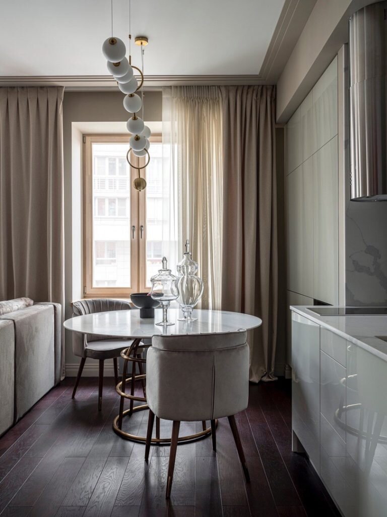 Основа интерьера — палитра нейтральных песочных оттенонков. Здесь есть и золотисто-песочный, и бежевый с фисташковым отливом, и сливочный, и даже лавандово-серый, оттеняющий теплые светлые оттенки. Но акцент этого интерьера — винный оттенок, который в разных интерпретациях встречается практически во всех помещениях квартиры. В зоне кухни сложно н обратить на пол с паркетной доской цвета благородного бордо.