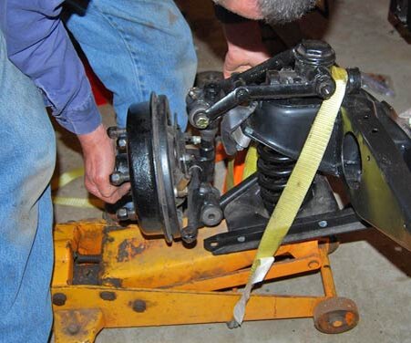 Крепежный ремень вокруг домкрата надежно удерживает рычаги A и цилиндрическую пружину в их надлежащих положениях, поэтому механик может установить нижний конец шпинделя и вставить новый штифт в отверстие для болта в нижнем рычаге A.