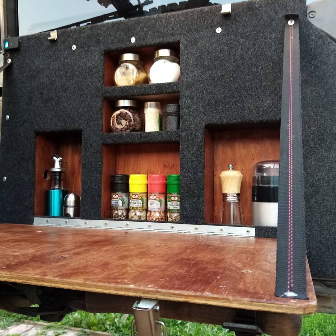 Вместо родной панели в двери багажника была выпилена передняя стенка и изготовлен короб из фанеры. После фанера была покрыта лаком, а недавно переднюю панель я обклеил карпетом. Также был изготовлен откидной столик для приготовления и быстрых перекусов при отдыхе. 