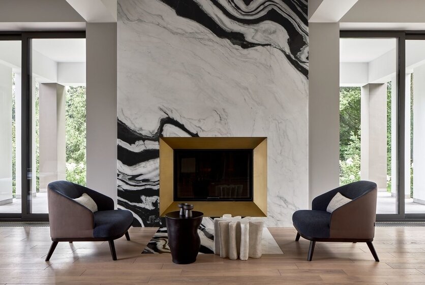 Каминнаязона. На приглушенном, пастельном фоне выделяется очаг, обрамленный латуннымпорталом и мрамором Panda White сконтрастным рисунком и выступающий ярким акцентом и фокусной точкой зоныкухни-гостиной. Кресла, Ditre Italia.Столики, Savour Design.