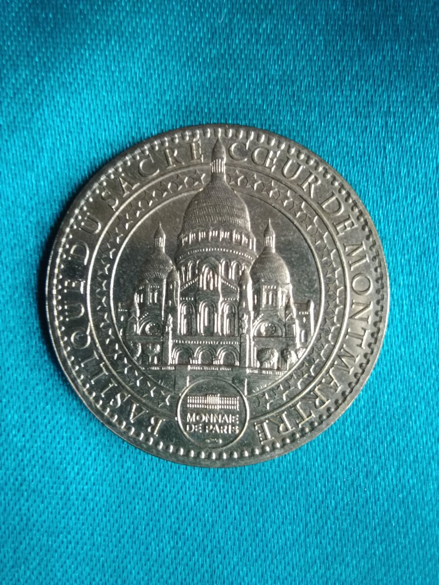   Аверс сувенирной монеты. На ней изображена Базилика Сакре -  Кёр. По кругу идёт надпись на французском языке. что в переводе на русский язык гласит: "Базилика Святого Сердца Монмартр". Внизу, в небольшом круге, изображено здание   и под ним надпись, в переводе на русский язык - Парижский монетный двор.                                                           