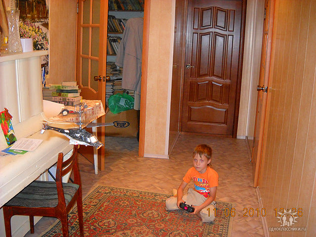 Радиоуправляемый вертолёт в полёте. Невдалеке сидит его малолетний пилот. 