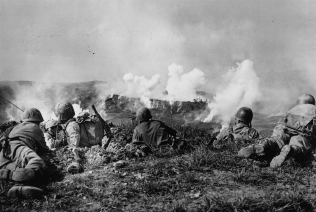 31 мая 1945 года: Американские морские пехотинцы из 1-й дивизии ждут на гребне холма в южной части Окинавы, наблюдая за взрывами фосфорных снарядов над японскими солдатами, окопавшимися в холмах.