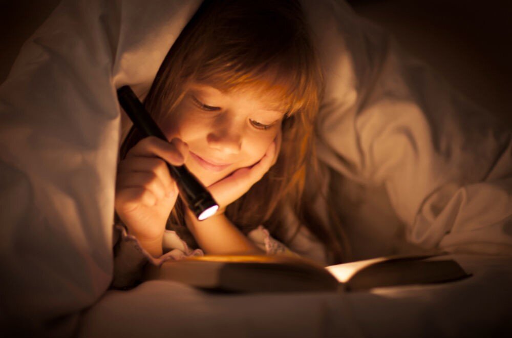 Ночью делают уроки. Чтение в темноте. Чтение под одеялом с фонариком. Дети под одеялом с фонариком. Чтение при плохом освещении.