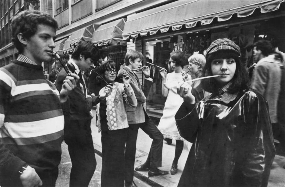 Модные молодые лондонцы курят трубки и сигареты в длинных держателях на улице Сохо в 1965 году.