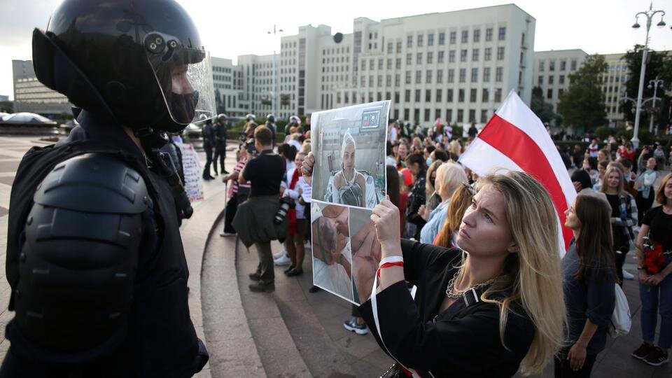 Протестующий в Минске противостоит сотруднику ОМОНа с фотографиями раненого.