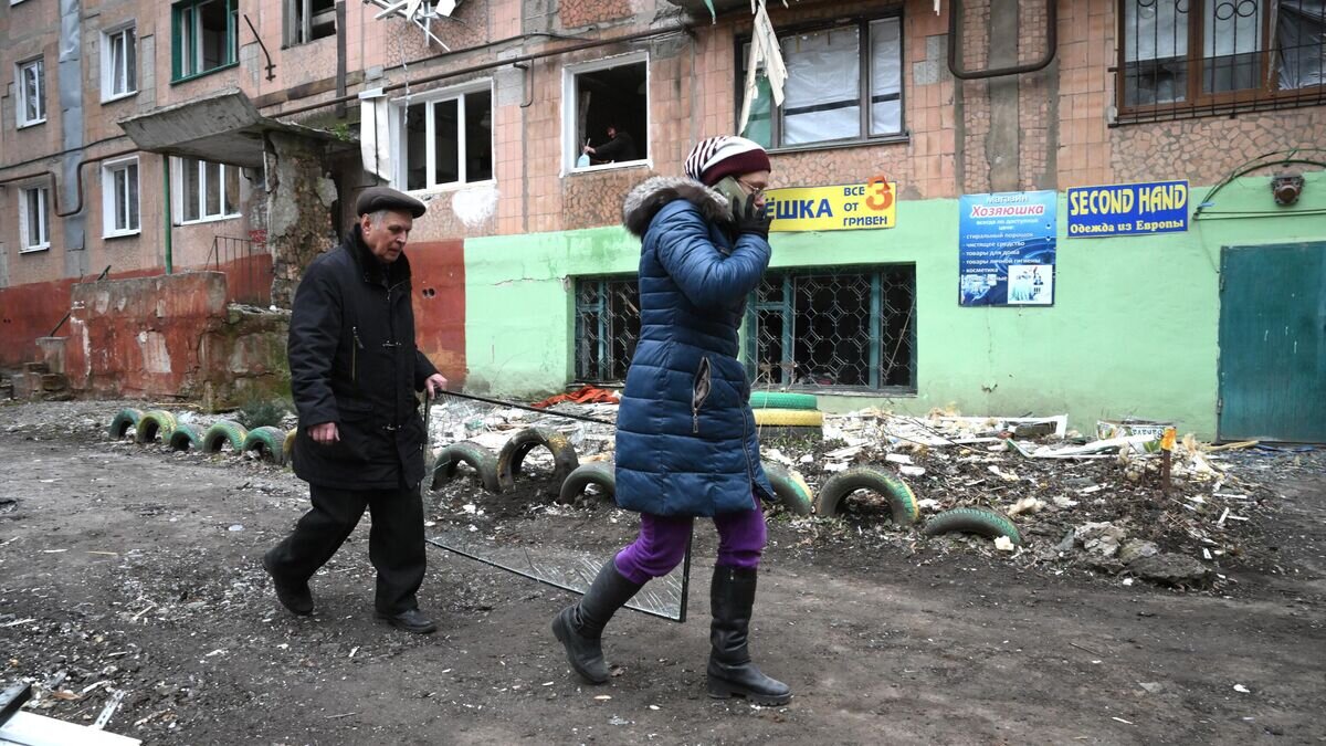    Люди идут вдоль дома, пострадавшего в результате обстрелов Горловки© РИА Новости / Илья Питалев