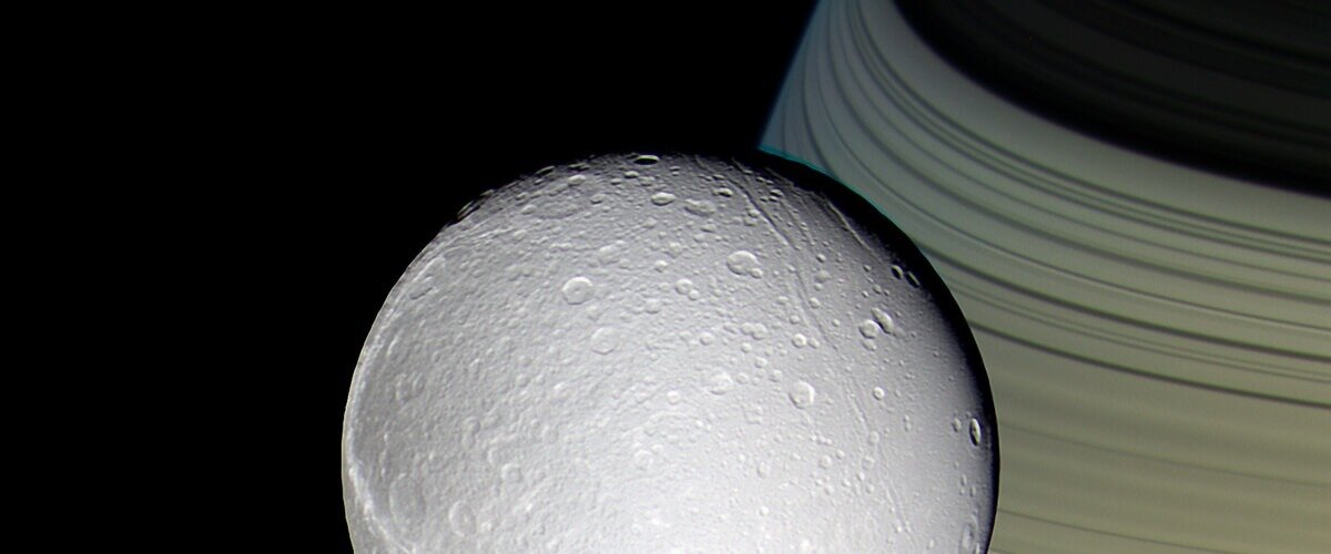 Диона на фоне колец Сатурна. Источник  НАСА