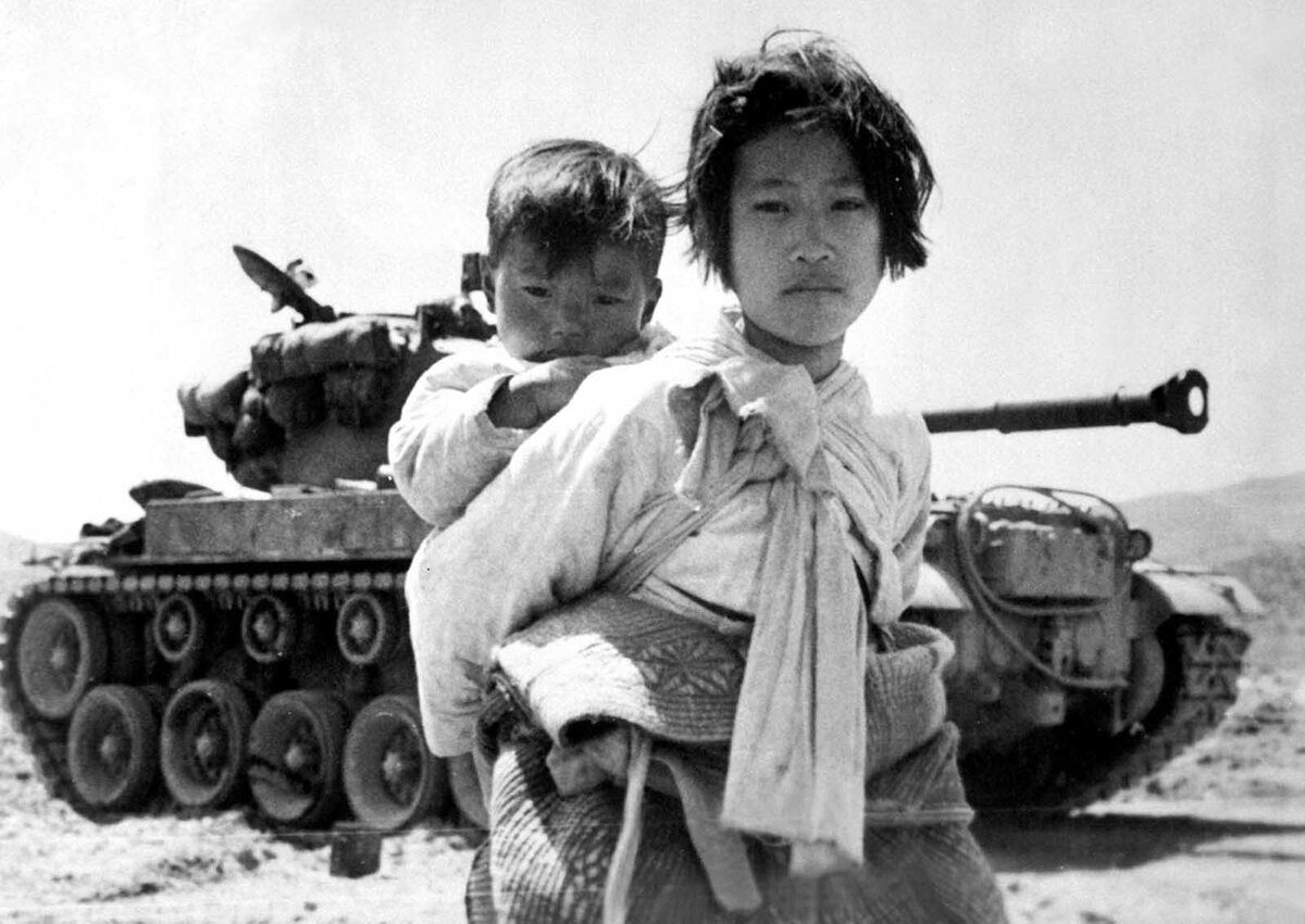 Утомленная войной кореянка с братом на спине пробирается мимо остановившегося танка М-26 в Хэнджу, Корея.  9 июня 1951 г.