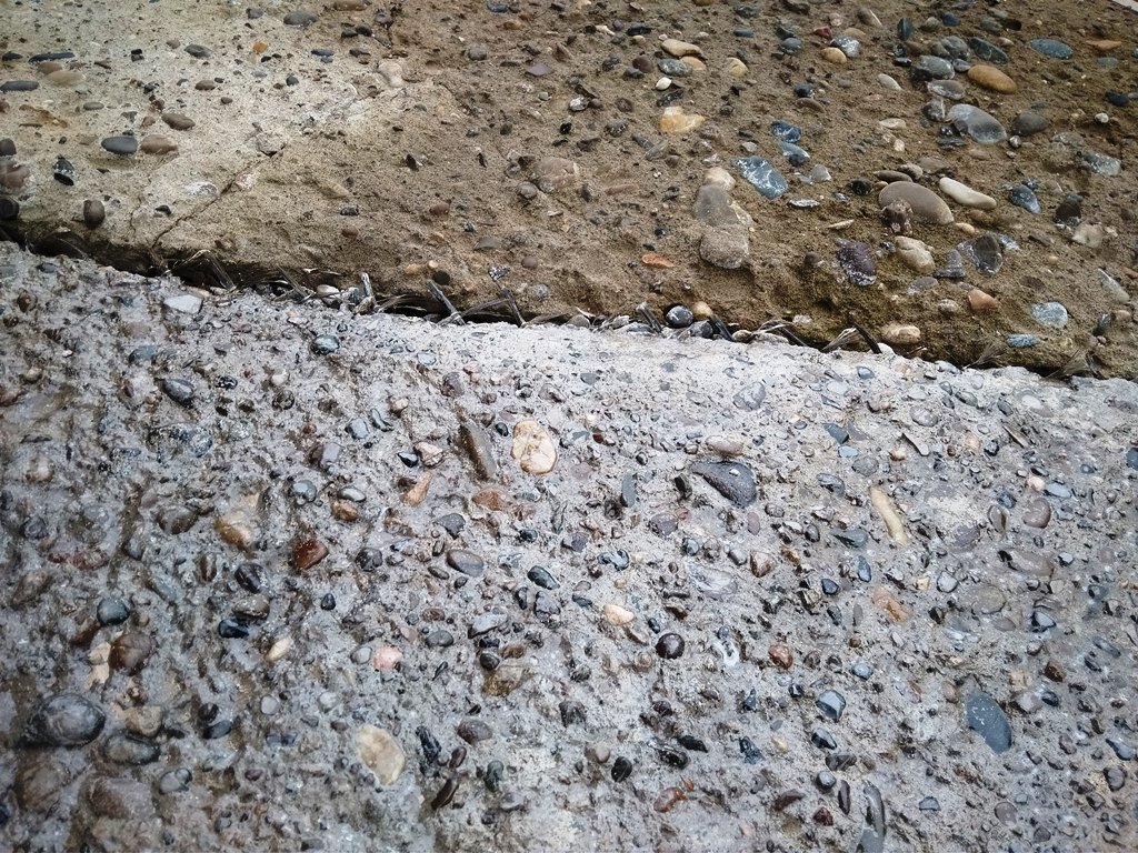 На фото нижняя половина отмостки покрыта лаком из пенопласта и ксилола, а верхняя часть отмостки пока без пропитки и видно что поверхность сильно разрушена