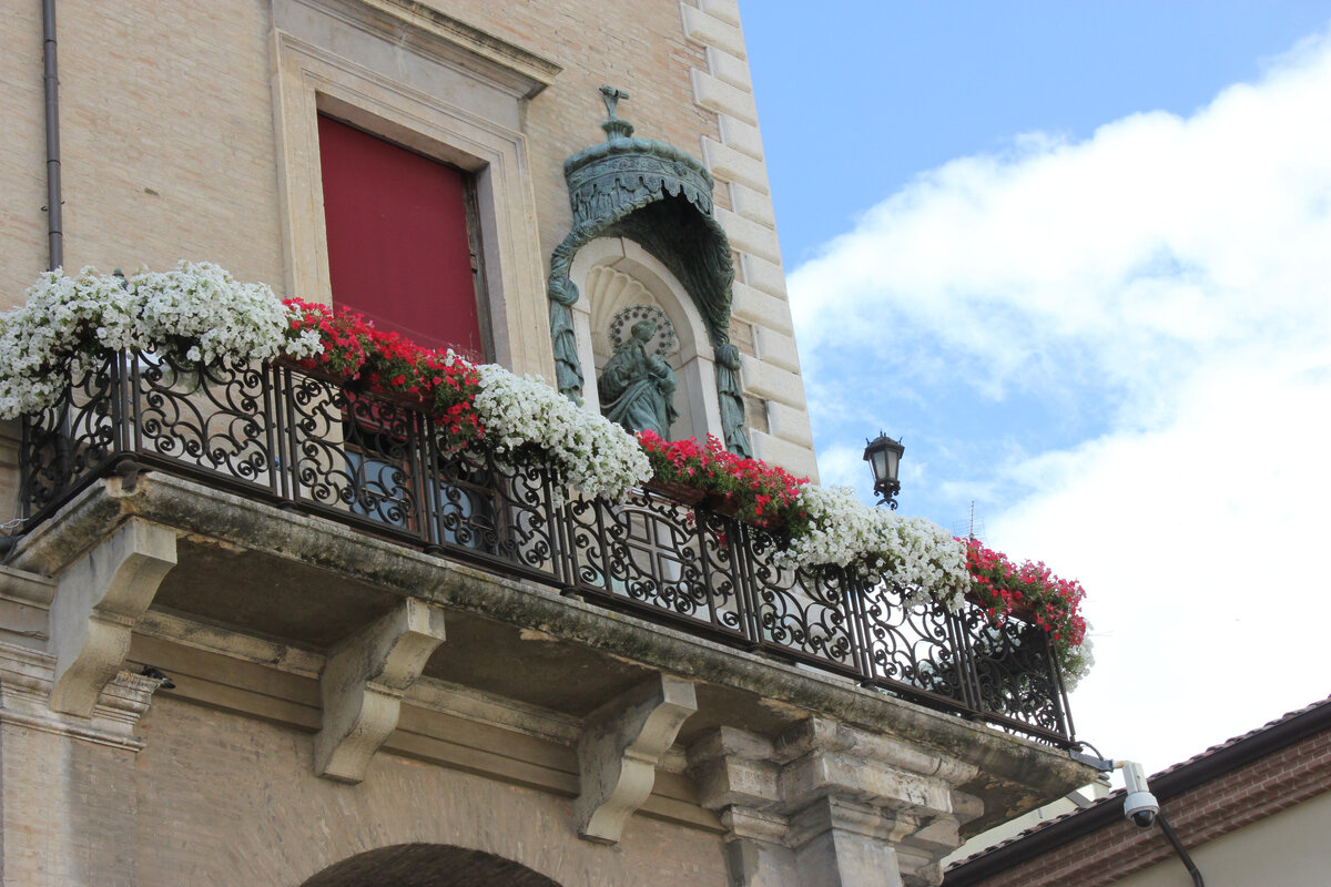 Италия. Римини. Красивый. украшенный цветами балкон и скульптура Пресвятой Девы.