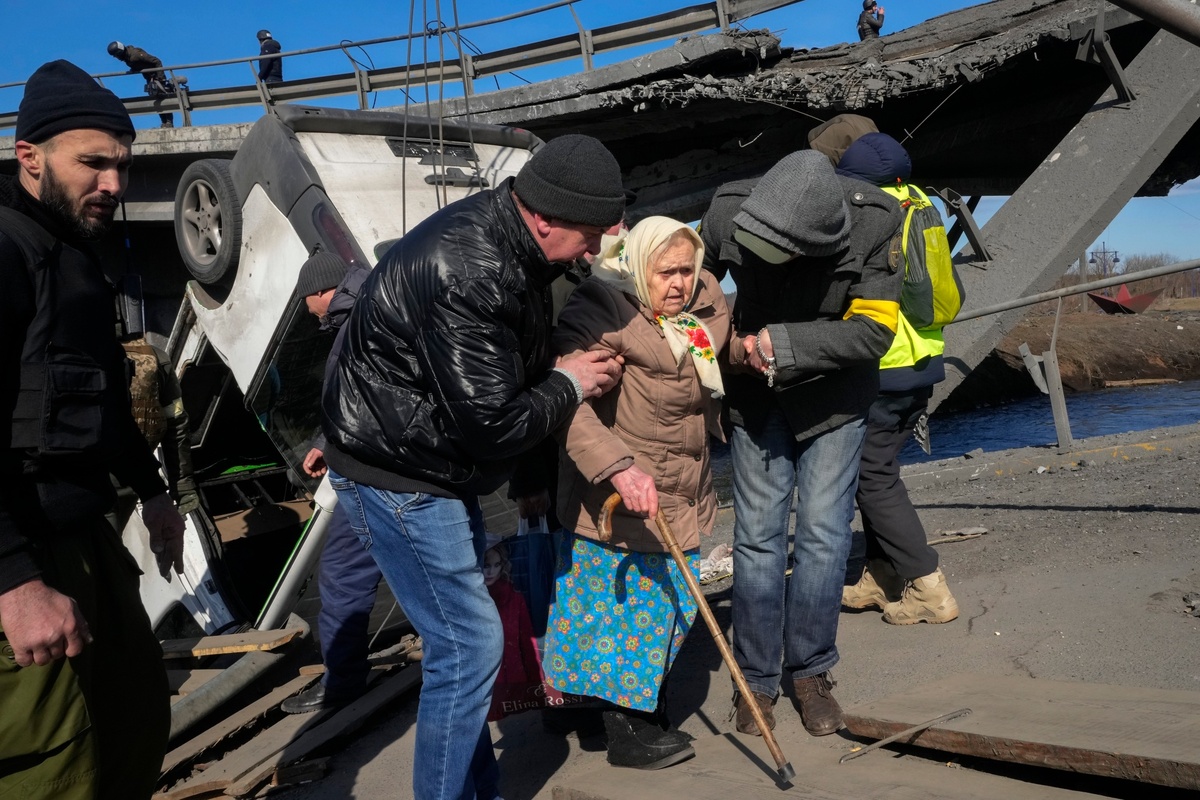 Волонтеры проходят импровизированную тропу под разрушенным мостом, эвакуируя пожилого жителя Ирпеня, примерно в 25 километрах к северо-западу от Киева, 11 марта.