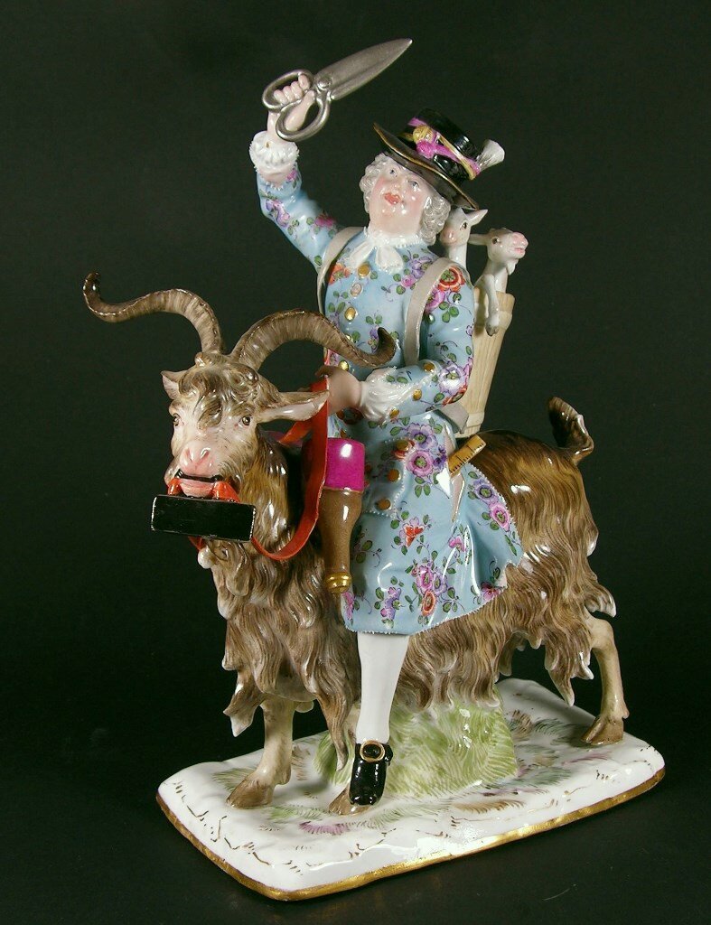 В данной статуэтке определить профессию седока нетрудно. Хотя бы по ножницам, поднятым в руке, как сабля, и по утюгу (однако не каждый зритель примет этот параллелограмм с ручкой за утюг), что держит козёл в своей пасти, как собака. Наряд явно не дворянина, а то, что называется, черни (хоть и разбогатевшей). Абсурда добавляет корзинка с козлятами, что держится на лямках за спиной седока. Листаем галерею, дабы рассмотреть второй вариант.