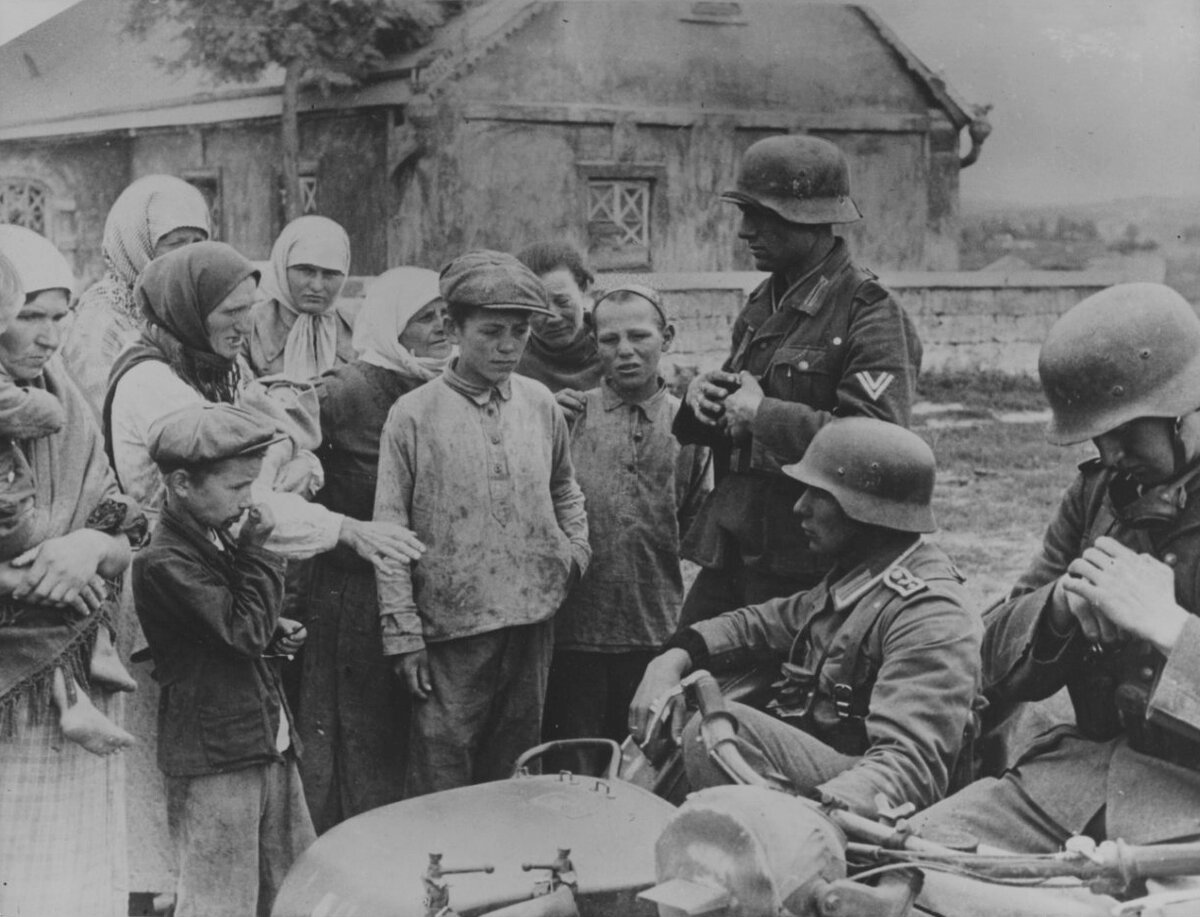 Пожилая жительница советской деревни что-то говорит сидящему в коляске мотоцикла обер-фельдфебелю вермахта / waralbum.ru