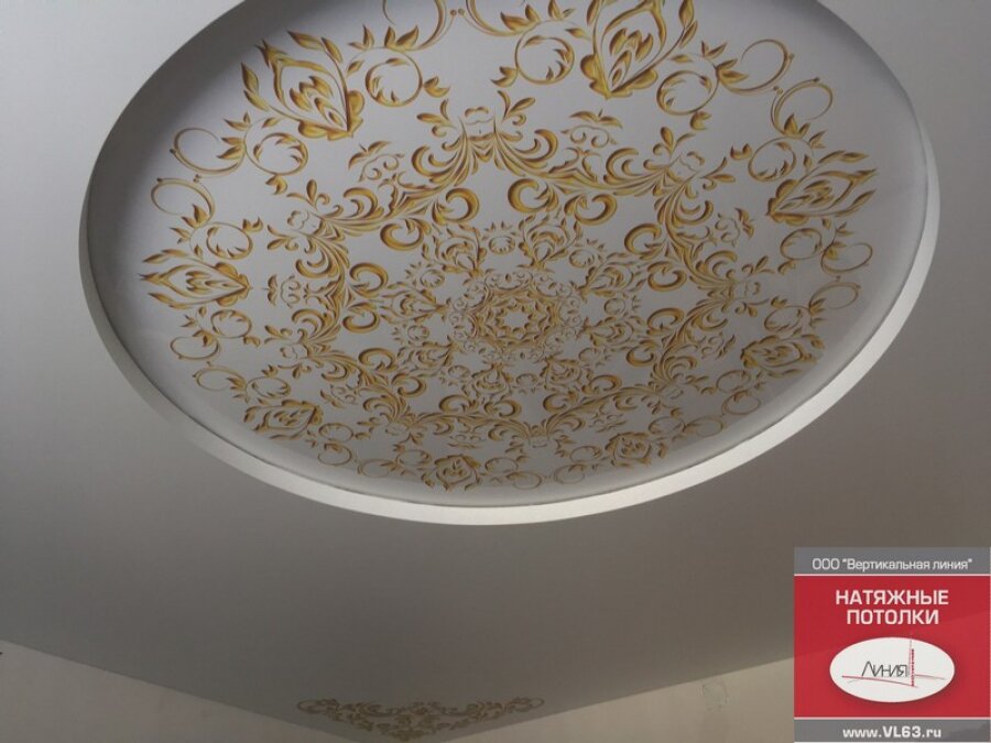 Двухуровневый белый натяжной потолок с золотыми орнаментами в центре и по углам.