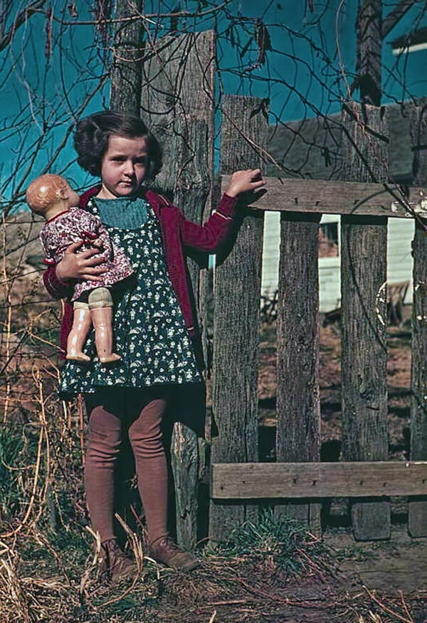 Девочка стоит у забора с куклой в руке. Местоположение не указано. Около 1941–1942 гг. / Библиотека Конгресса