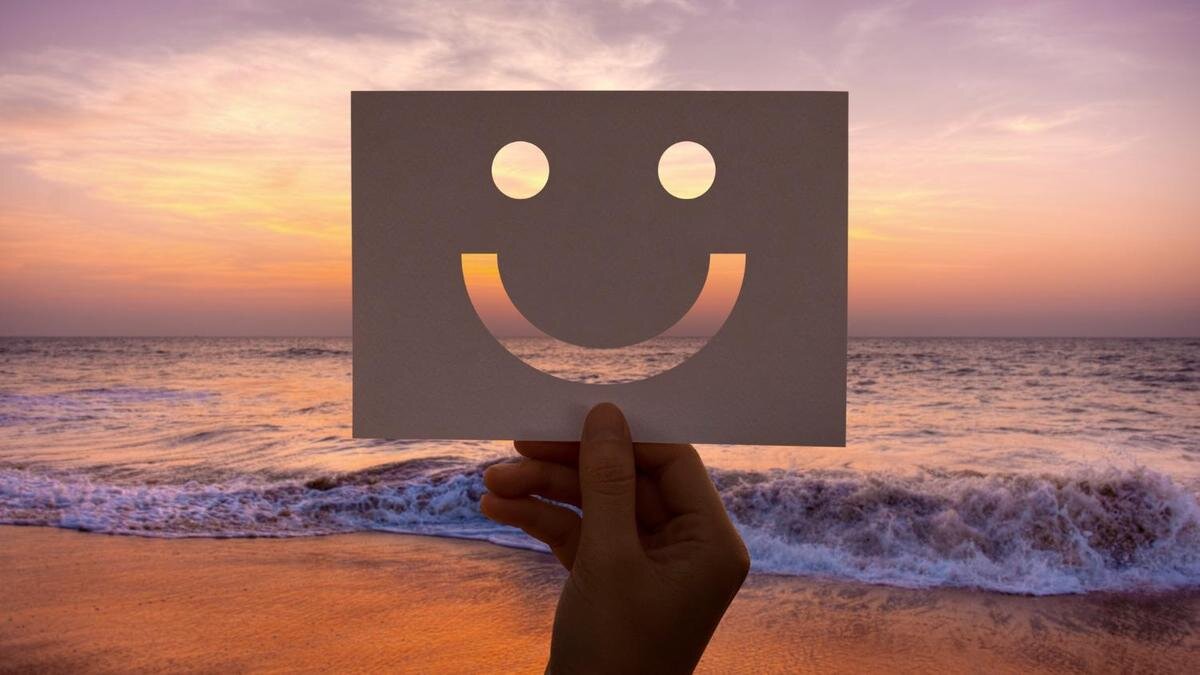    Лист бумаги, в котором вырезана счастливая рожица, на фоне моря:Freepik