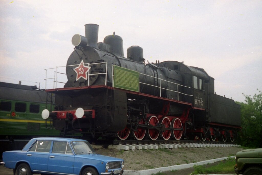 Паровоз Эу677-33. Депо Тула 1998 год. Паровоз выпущен в Брянске в 1928 году. Установлен как памятник 22 апреля 1978 года. По словам работников депо, прибыл в Тулу для установки в качестве памятника из существовавшего в то время депо Черепеть. В настоящее время этот паровоз-памятник по-прежнему на своем месте, разве что серп и молот на звезде исчез. Приметы времени на фото – ВАЗ-2101 на переднем плане и капот УАЗ-469.