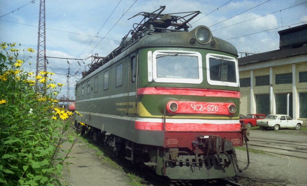 ЧС2-826 приписки Москва-Пассажирская-Курская в депо Тула, 2000 год. На заднем плане аналогичные артефакты времени – припаркованные личные автомобили работников- Москвич-2140 и Волга ГАЗ-2410. За ними угадывается «зубило» ВАЗ 2108 или 2109. Электровоз ЧС2-826 начал свою службу в депо Харьков-Октябрь, в 2003 был модернизирован в ЧС2К и передан в депо Москва-Сортировочная, в 2015 поставлен в запас в 2018 утилизирован.