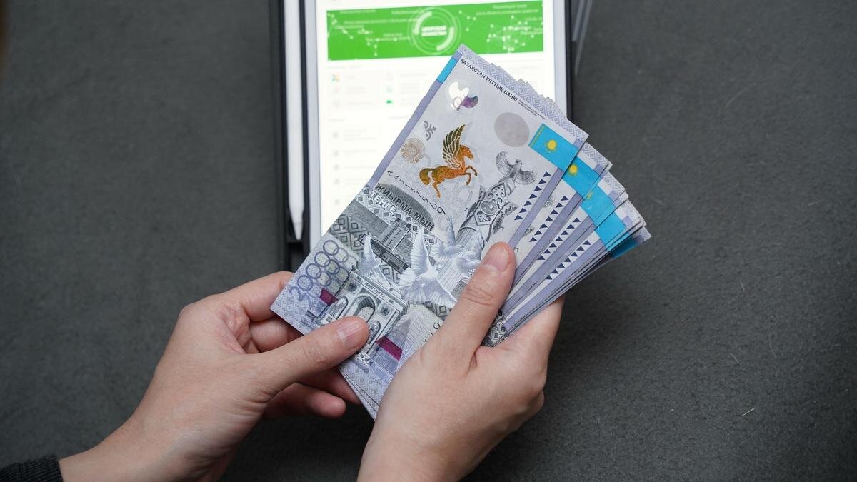    Женщина держит пачку денег на фоне планшета:NUR.KZ / Владимир Третьяков