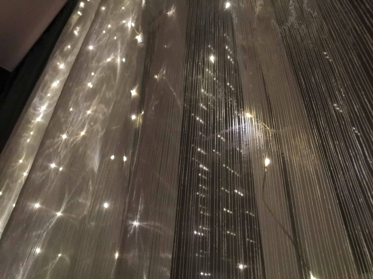 Тонкие проволочки гирлянды на фоне тюля практически незаметны