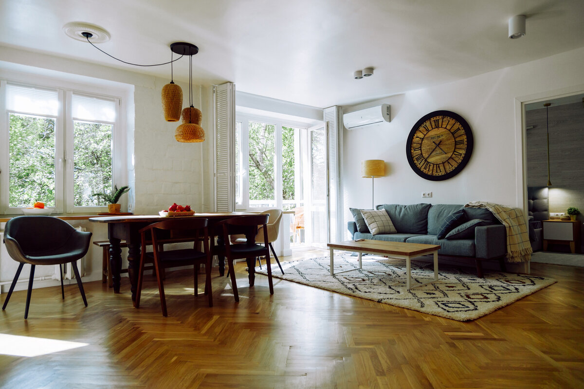 Так сейчас выглядит гостиная. Общая площадь комнаты — 30 квадратных метров. За счет нескольких окон и белых стен пространство расширяется и кажется еще больше, чем есть на самом деле. В центре гостиной стоит обеденный стол, за которым можно собраться всей семьей. Но моя самая любимая деталь в этом интерьере — роскошный восстановленный паркет