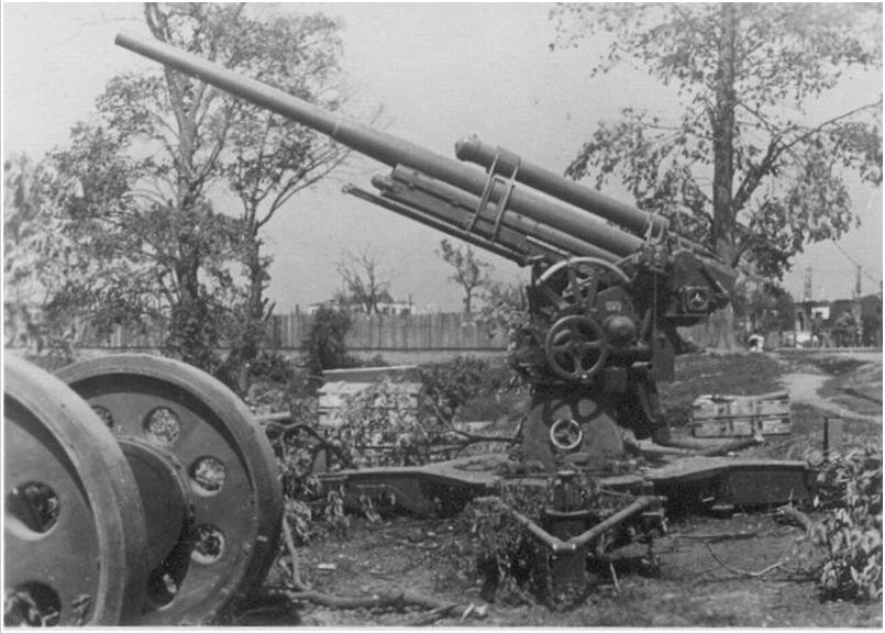 Зенитное орудие обр. 1931 года, видны маховички вертикальной наводки, с другой стороны пушки расположено креслице горизонтального наводчика на переднем фоне колесный ход, само орудие в боевом положении на платформе.