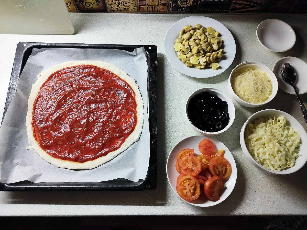 Смазанная соусом основа для пиццы и мизанплас (т.е. раскладка подготовленных ингредиентов) 