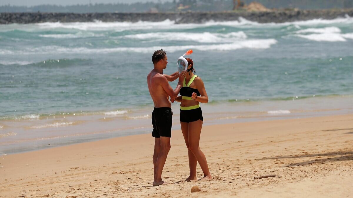    Мужчина помогает женщине надеть маску для сноркелинга в Хиккадуве, Шри-Ланка© AP Photo / Eranga Jayawardena