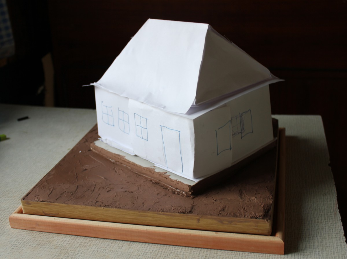 Моделист начал работу над диорамой с создания бумажного макета дома. Дом - это крупное сооружение и занимает большинство места на диораме. Основание выполнено на большом квадратном основании размером 40х40 см. Снизу-лист гипсокартона. Нанесена коричневая акриловая шпаклевка 