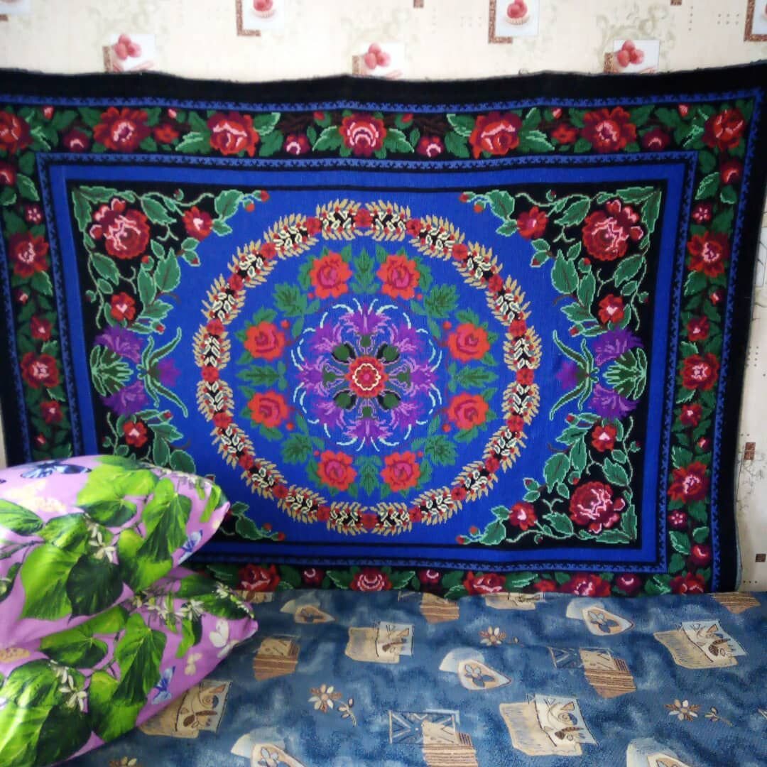 У моей бабушки в деревне на стене дома висит красивый ковёр вышитый её руками. Этот ковёр был вышит ею более 20 лет назад. Для изготовления данного ковра она использовала ненужные разноцветные вещи. Бабушка вязала варежки, носки шарфы платки и кофты. Но теперь из-за возраста она уже не вяжет. Вечера бабушка проводит сидя у телевизора смотря любимые сериалы