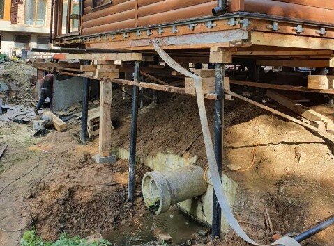 Делается отвод грунтовых вод, подъём строения, монтаж винтовых свай