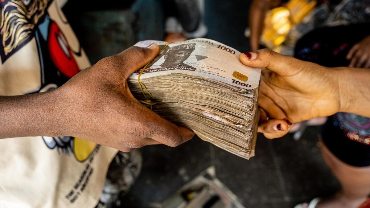    Мужчина передает пачку денег из рук в руки:Damilola Onafuwa/Bloomberg via Getty Images