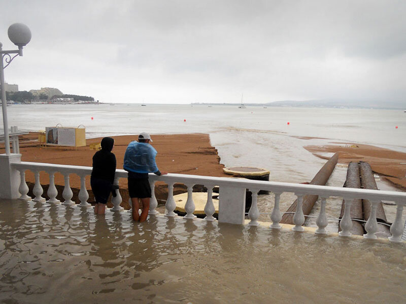 Остатки водя стекают с набережной в море, размывая песок на пляже.