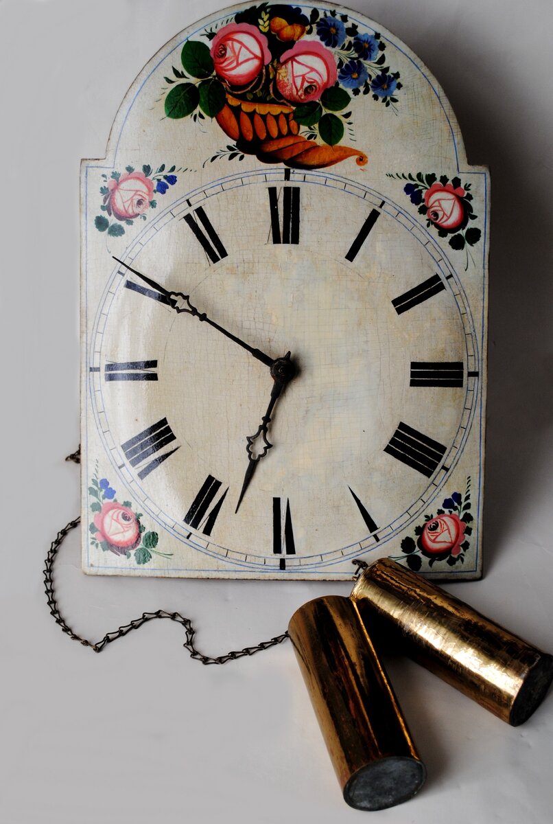 Раритетные часы середины 19 века, интересный экземпляр, отражающий историческую, культурную эпоху дореволюционной России, являются частью сформировавшейся моды середины 19 века!  
Это деревянные гиревые настенные часы-ходики, с ручной цветочной росписью по левкасу, с механизмом на деревянных платах. Настенные часы к XIX веку стали ключевым объектом обстановки, постепенно приобретая большую популярность по сравнению с огромными, занимающими много места напольными маятниковыми часами. Настенные часы можно было встретить в солидной городской квартире, загородной усадьбе, они присутствовали в рабочем кабинете, столовой и гостиной, спальной комнате. Они были различной формы и стилевого решения: классические, в деревянном полированном корпусе, с простыми формами или резными деталями, либо украшенные в античном стиле, встречались роскошные большие часы с бронзовыми золочеными накладками, часы с оформлением декора в рокайльном стиле. К 1830-м гг. в эпоху нового интерьерного стиля «бидермейер» большую популярность приобретают компактные, легкие настенные часы, простой формы – провинциальные ходики. В быту их называли «ходунцами» и «ёкальщиками». Они были недорогими, простыми в изготовлении. Их можно смело отнести к российскому производству, назвать «народными», «русскими». Вплоть до начала XX века изготовление часов в России практически полностью зависело от иностранных поставок. Как таковой часовой промышленности в широком понимании не было; существовало сборочное производство часов из ввозимых деталей. В первой половине XIX века, вслед за открытием часовой школы в Петербурге, повсеместно появляются мелкие часовые мастерские. Производство часов было кустарным. Часовщики собирали механизм при мастерских. Самое крупное производство часов-ходунков располагалось в Москве и Подмосковье. Известно, что в первой половине XIX века начало такому производству «местных» часов положил Гаевский Петр Лазаревич, бывший крестьянин, впоследствии купец третьей гильдии, который объединил всех кустарей-часовщиков в Москве. Гаевский участвовал во многих промышленных выставках, его изделия награждались серебряными медалями за общедоступность и простоту настенных часов. Часы-ходунки стоили не более 50-80 копеек (средняя зарплата рабочего в середине XIX века составляла приблизительно 18-20 рублей). Производство часов-ходунков стало семейным делом Гаевских. Часы Гаевских примечательны были своей искусной росписью. Стоимость некоторых часов, расписанных женой Петра Лазаревича Авдотьей, доходила до 200 рублей, они получали высокую оценку известных часовщиков России того периода. После 1860-х годов производство часов-ходунков было сосредоточено преимущественно в деревне Шарапово Звенигородского уезда Московской губернии. Изделия мастеров Шарапово стоили дешевле своих предшественников, рисованные циферблаты заменялись печатными на бумаге; появились первые часы с корпусом из жести.

Корпус представленных на фото часов-ходунков украшен цветочным орнаментом по белому грунту. Узор нанесен прорисью, т.е. с помощью перевода рисунка со схематического наброска, контура, обратная сторона которого натиралась углем или графитом и придавливалась к «рабочей» поверхности; далее контуры процарапывались иглой и уже краской прорисовывались линии («графьи»). Стоит отметить, что роспись часов, а также орнамент на корпусе - цветочный декор – вполне традиционный для своего времени, отвечает тенденциям моды середины XIX века. Вообще так называемые «картинные часы» (декорированные живописным орнаментом, пейзажем и т.п.) были известны еще в XVII веке. Это была находка для любителей подчеркнуть интерьер, внести завершающую ноту в дизайн убранства. А сам растительно-цветочный орнамент как элемент декора всего жилища и предметов женского и даже мужского гардероба появляется еще в древних империях. Подобный узор являлся не только элементом моды, он нёс в себе сакральное значение. Первоначально цветочный принт нашел широкое применение именно в костюме; ткани, расшитые цветами, входят в моду с XIV века. Постепенно мода на цветы распространяется на все виды искусства. Но особо популярным цветочный декор стал в первой половине XIX века. На многих предметах интерьера и гардероба появляются целые букеты различных цветов. Большую роль в этом сыграла эпоха рококо, полюбившиеся цветы уверенно вошли в моду нового столетия. Большому спросу на флористический орнамент в эпоху «бидермейер» способствовало и развитие садоводства. 1820-1850- е гг. – это время открытий множества новых видов растений. В дворянских усадьбах появляются целые оранжереи из экзотических цветов. Появляются штамбовые, китайские, чайные розы различных форм и расцветок. Роза, как элемент декора, становится фаворитом в середине XIX века. Цветочные оранжерейные ковры начинают копировать на бытовые предметы, а отдельные элементы женского гардероба и вовсе напоминали клумбы. Цветник в декоре становится важным элементом русской культуры. Часы-ходунки в полной мере отвечают тенденциям интерьерной моды эпохи на легкость, простоту, пастельные, светлые оттенки, создавая общий вид провинциальности и уюта. К рубежу 19-20 вв. цветочный декор на часах постепенно вытесняется тематическим оформлением корпуса в виде «кошки» с бегающими в разные стороны глазами, с изображением сказочных персонажей. К 1920-1930-м годам коллекция российских часов пополнилась аналогичными предметами в жестяном корпусе и печатным изображением на советскую тематику.
Часы представлены из коллекции Пензенского Литературного музея.
https://vk.com/muzlitpenza