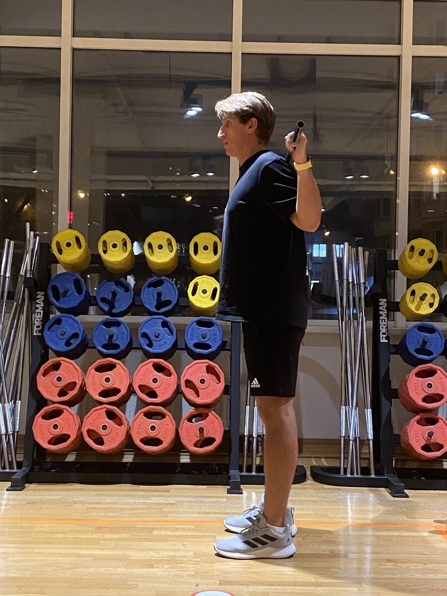 Встаньте прямо, ноги врозь на ширине плеч. Поместите гриф или палочку сзади в области верхней части спины ниже плеч, область трапеции. Сохраняя прямое положение спины, отводите таз назад синхронизируя со сгибанием коленей, см следующий слайд внизу.