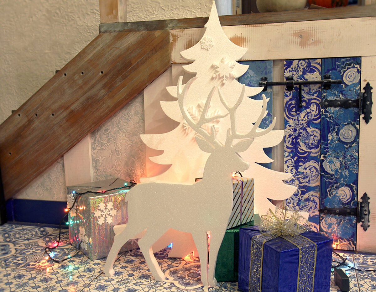 На фотографии фигура оленя из пенопласта, ёлка, снежинки и геометрические фигуры "Куб" оформленные яркой бумагой составляют новогоднюю композицию.