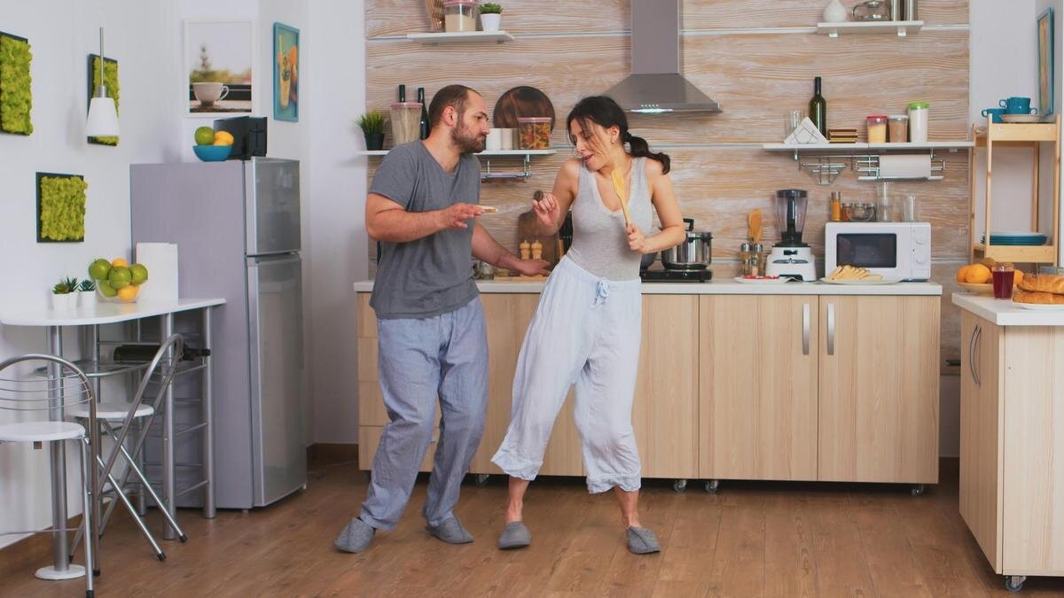    Мужчина и женщина в домашней одежде танцуют на кухне:Freepik