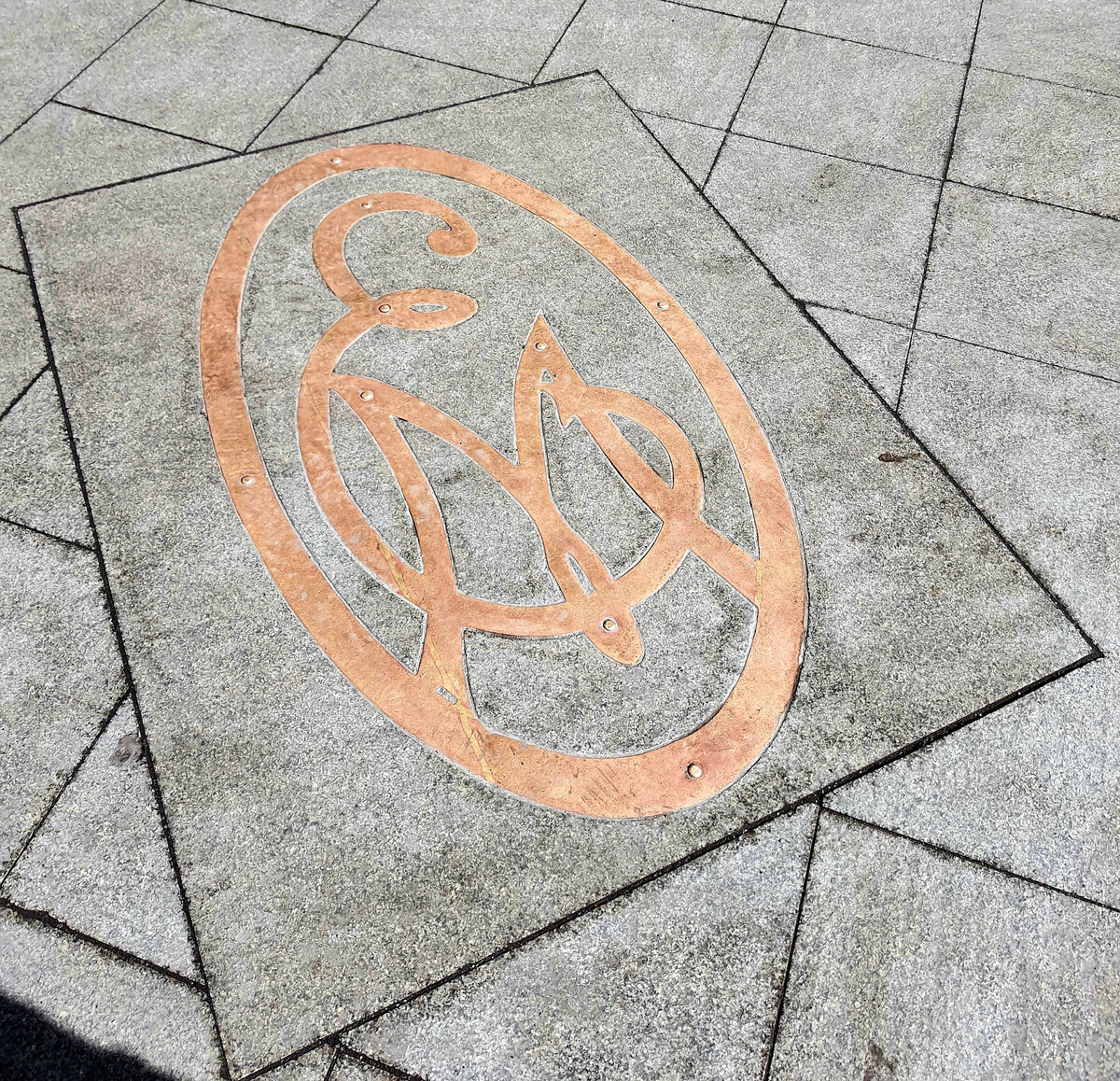 Эмблема магазина в тротуарной плитке напротив входа.