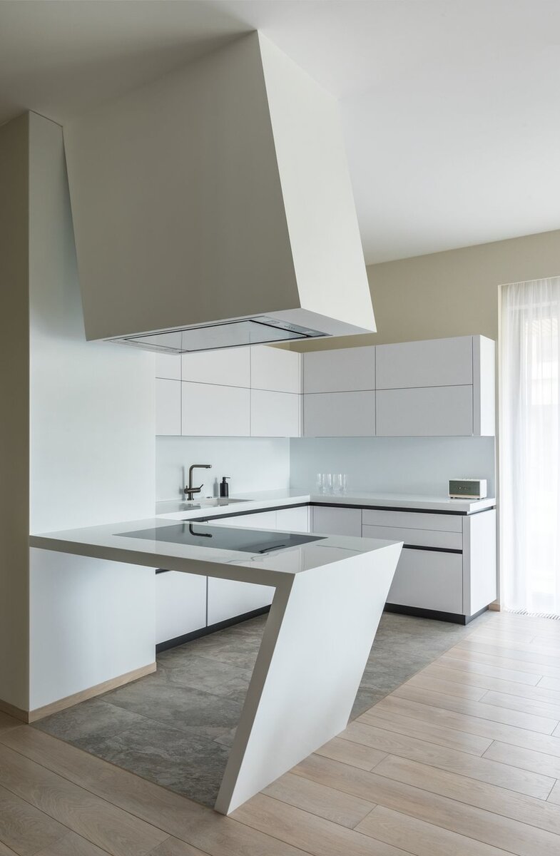 Угловую форму кухонного острова со встроенной варочной панелью поддерживает вытяжка, оборудованная в ассиметричном объеме, нависающем сверху. Монументальная композиция добавляет пространству динамики. Авторы проекта: Екатерина Мещанова, Анатолий Тюрин. Фото: Михаил Степанов