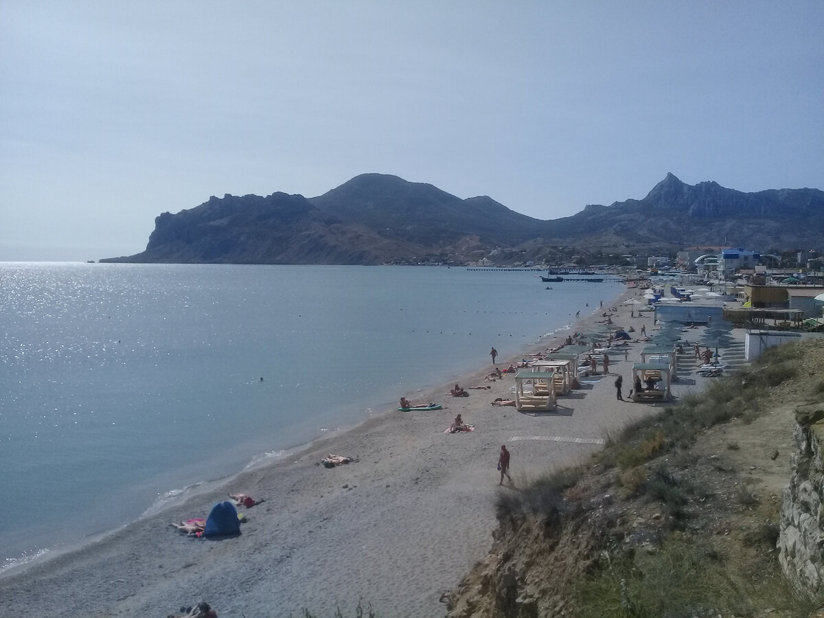 У северо-восточного подножия массива Карадаг лежит курорт Коктебель. Пляж в Коктебеле. Вулкан Карадаг на горизонте.