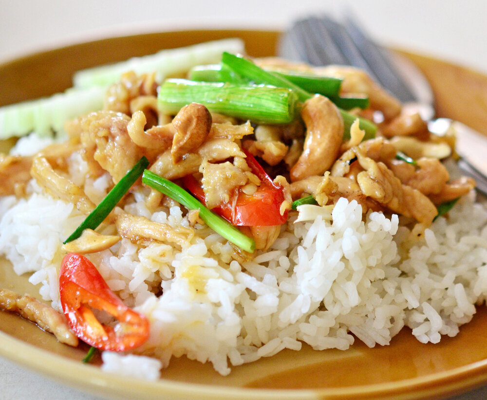 Ингредиенты Соус: 
1/2 стакана (120 мл) хойсина 
1/2 стакана (120 мл) куриного или овощного бульона 
1/4 стакана (60 мл) соевого соуса с низким содержанием натрия или тамари 
1/4 стакана (60 мл) меда или агавы 
2 столовые ложки (30 мл) рисового уксуса 
1 столовая ложка (15 мл) шрирача по
1 шт. Или 1/4 стакана (40 г) лука-шалота, очищенного и измельченного по 
2 шт.  (10 г) очищенных и измельченных зубчиков чеснока 
1 чайная ложка (3 г) имбиря , очищенные и измельченные 

Блюдо:
2 чайные ложки (10 мл) оливкового масла первого холодного отжима 
4 каждой (500 г) куриных грудок без кожи и костей, нарезанных небольшими кусочками
1 1/2 стакана (200 г) красного болгарского перца, очищенного от семян и нарезанного кубиками 
1 1/2 стакана (200 г) зеленого болгарского перца, очищенного от семян и нарезанного кубиками 
3/4 стакана (100 г) кешью 
1 стакан (170 г) коричневого риса
2 стакана (500 мл) воды 
1 чайная ложка (2 г) семян кунжута 

Подготовка 

В большой миске взбейте венчиком, чтобы смешать хойсин, бульон, соевый соус, мед, уксус, шрирача, лук-шалот, чеснок и имбирь. 
Нагрейте большую сковороду или вок на среднем или сильном огне. Когда все станет горячим, добавьте масло и перемешайте, чтобы покрыть дно. Добавить курицу и перец, жарить, помешивая, 2-3 минуты, пока курица слегка не поджарится, а перец не начнет размягчаться. 
Добавьте соус и орехи кешью, перемешайте и доведите до кипения. Продолжайте варить на медленном огне, пока курица не будет полностью приготовлена, а соус не превратится в тонкую глазурь, 12-15 минут. Держите в тепле, пока не будете готовы к подаче. 
Пока курица готовится, поместите рис и воду в кастрюлю среднего размера. Доведите воду до кипения на среднем или сильном огне. После закипания уменьшите огонь до средне-слабого, накройте крышкой и готовьте 18-20 минут (или в соответствии с инструкциями на упаковке) до готовности. Дайте настояться, приоткрыв крышку, на 5 минут. 
Перед подачей разделите рис и курицу по тарелкам или мискам и посыпьте кунжутом. 